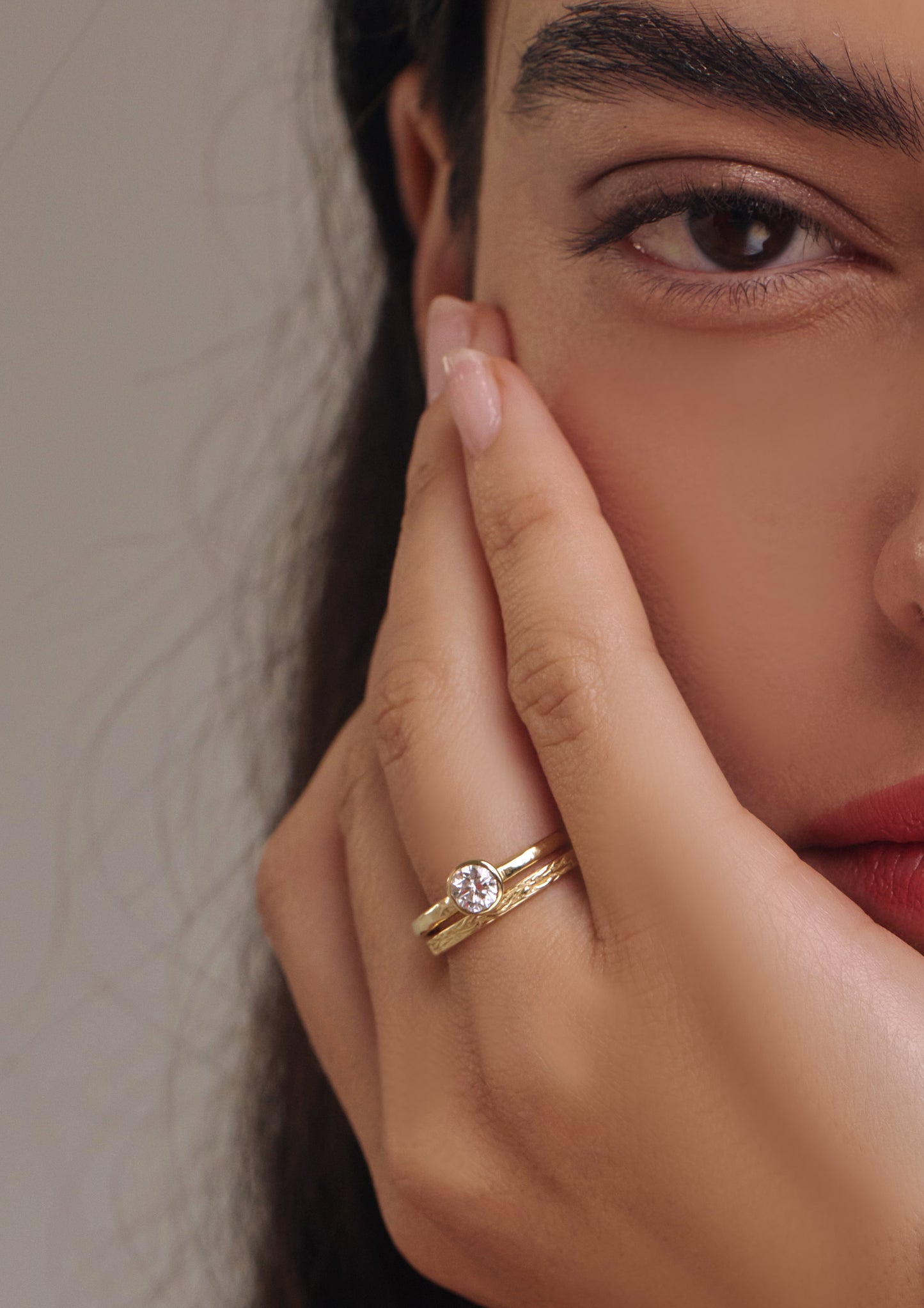 Close-up of a hand wearing a gold engagement ring with a diamond, touching the cheek.